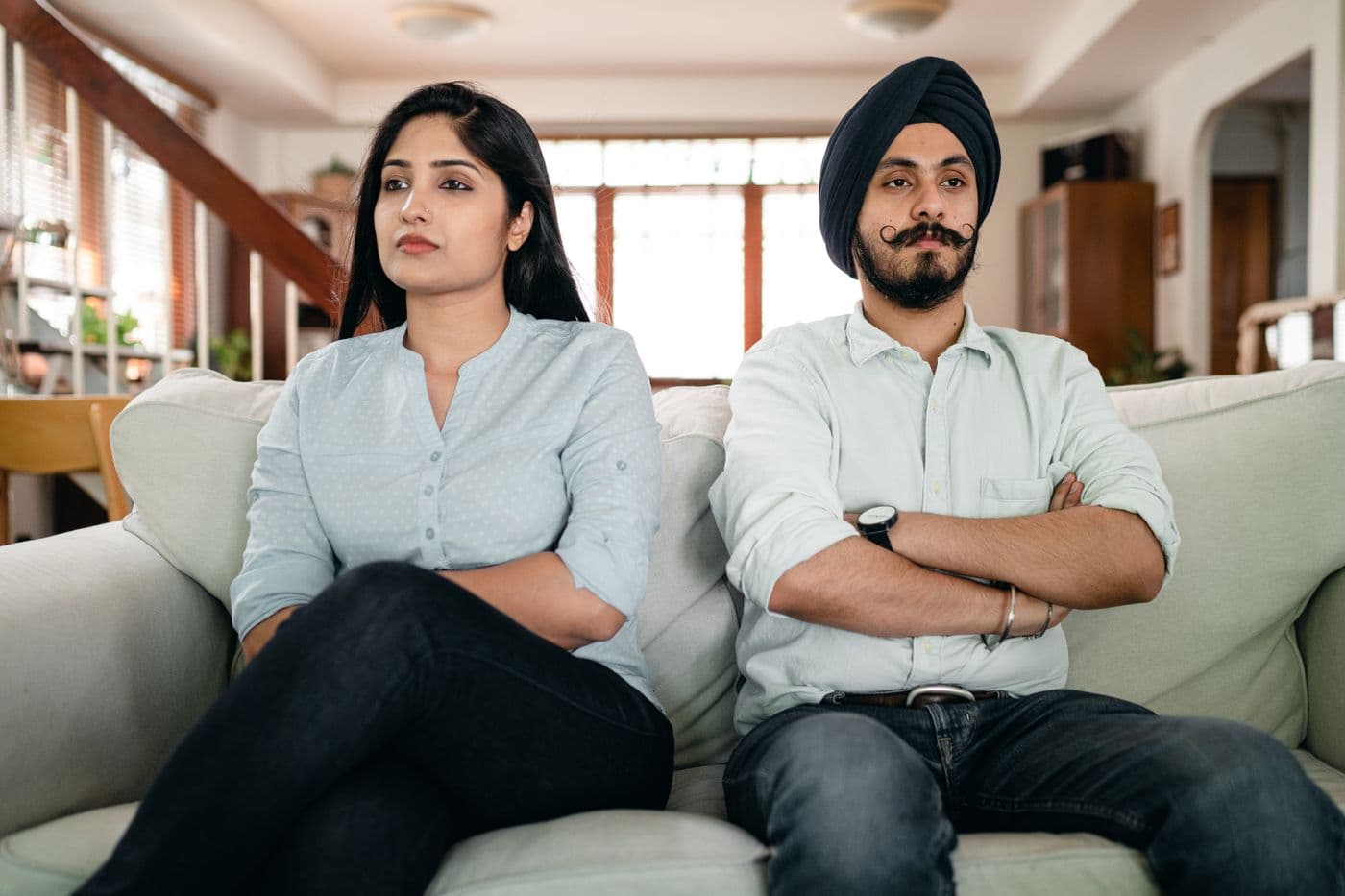 A couple sitting apart on a sofa, arms crossed, not looking at each other.