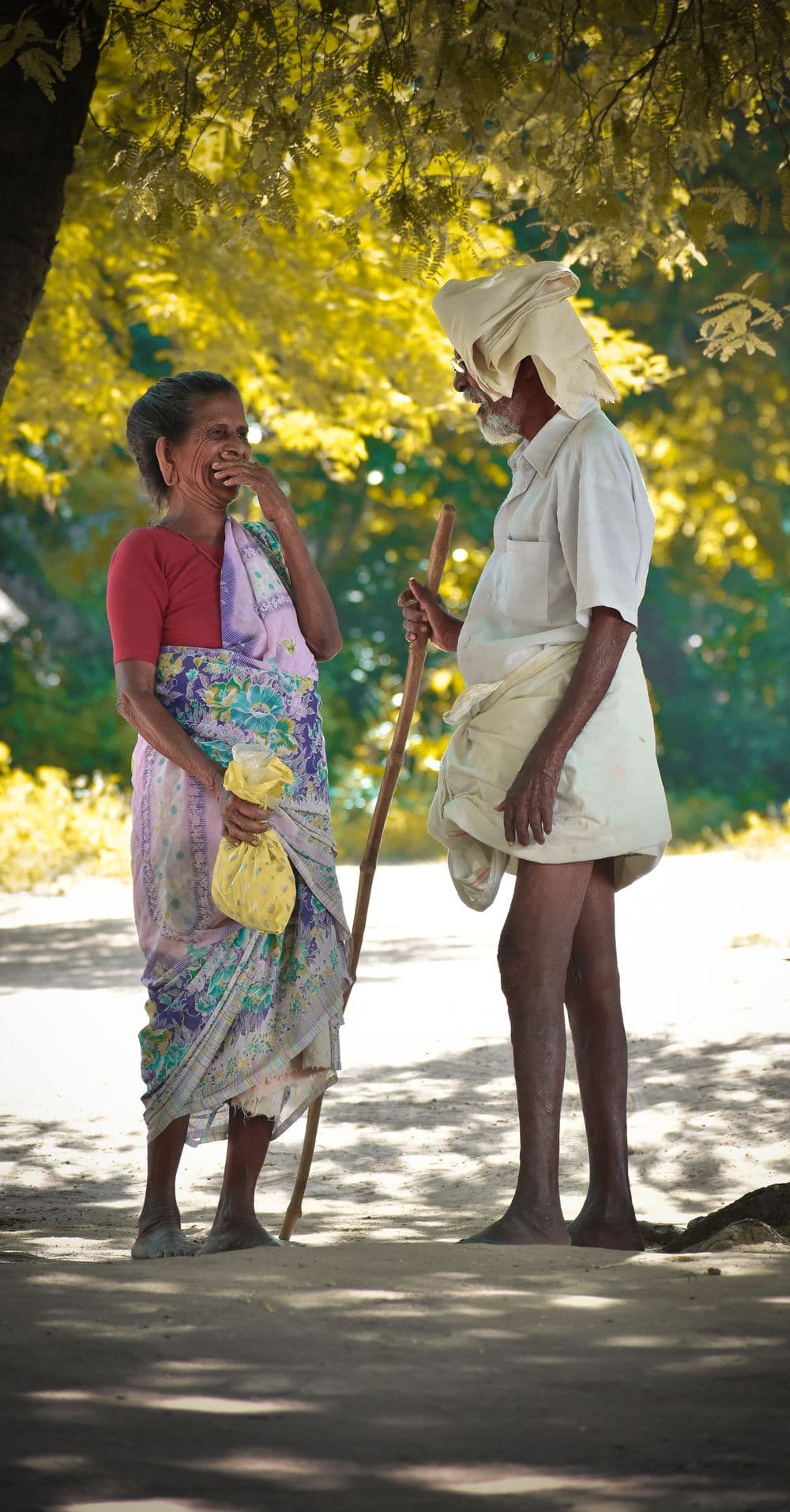 An older couple laughing together under the trees.