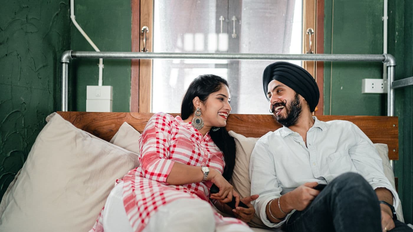 A couple laughing together on a sofa, turned toward each other.