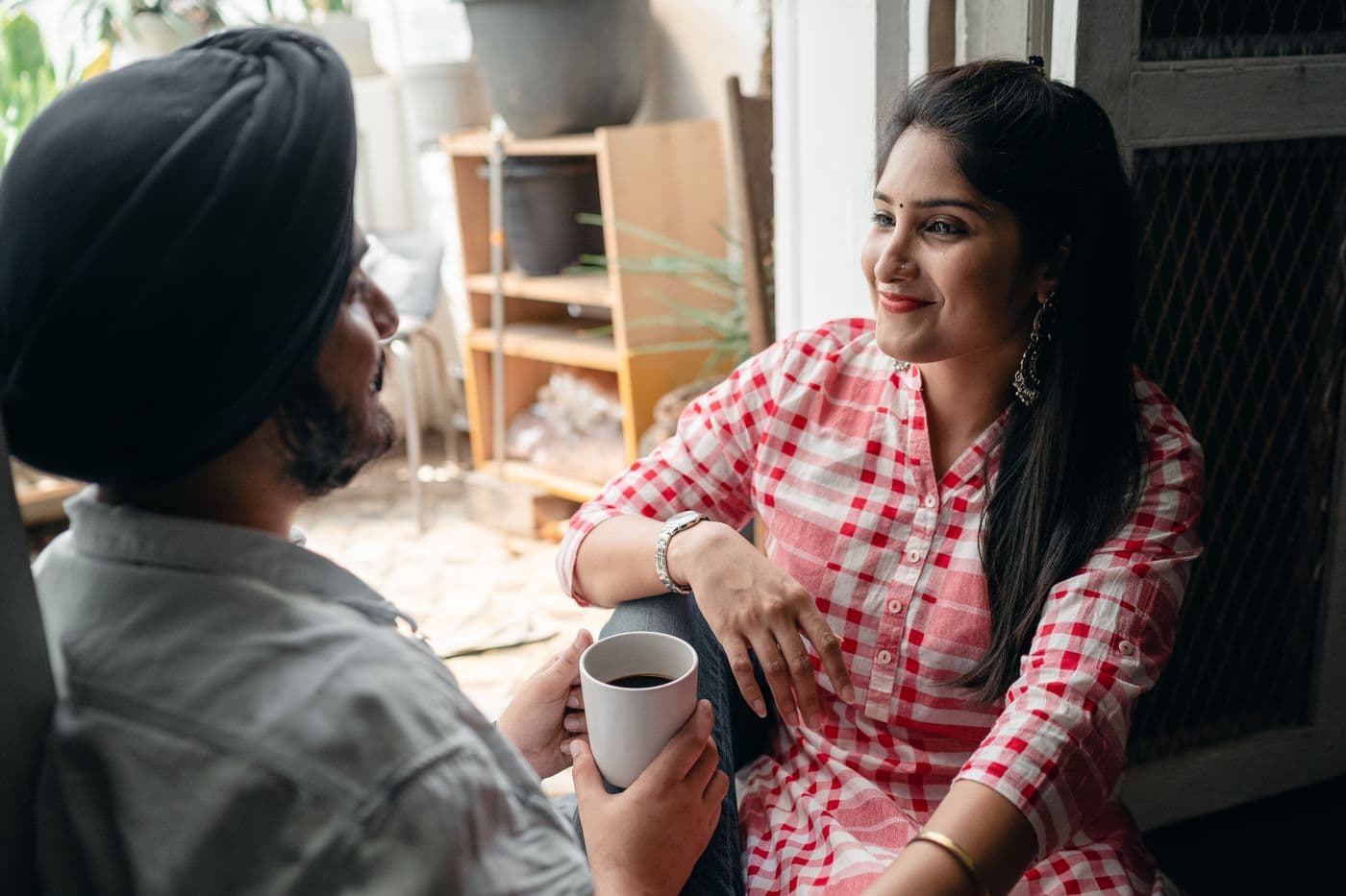 A couple sharing tea in a sunny doorway, smiling as they talk.